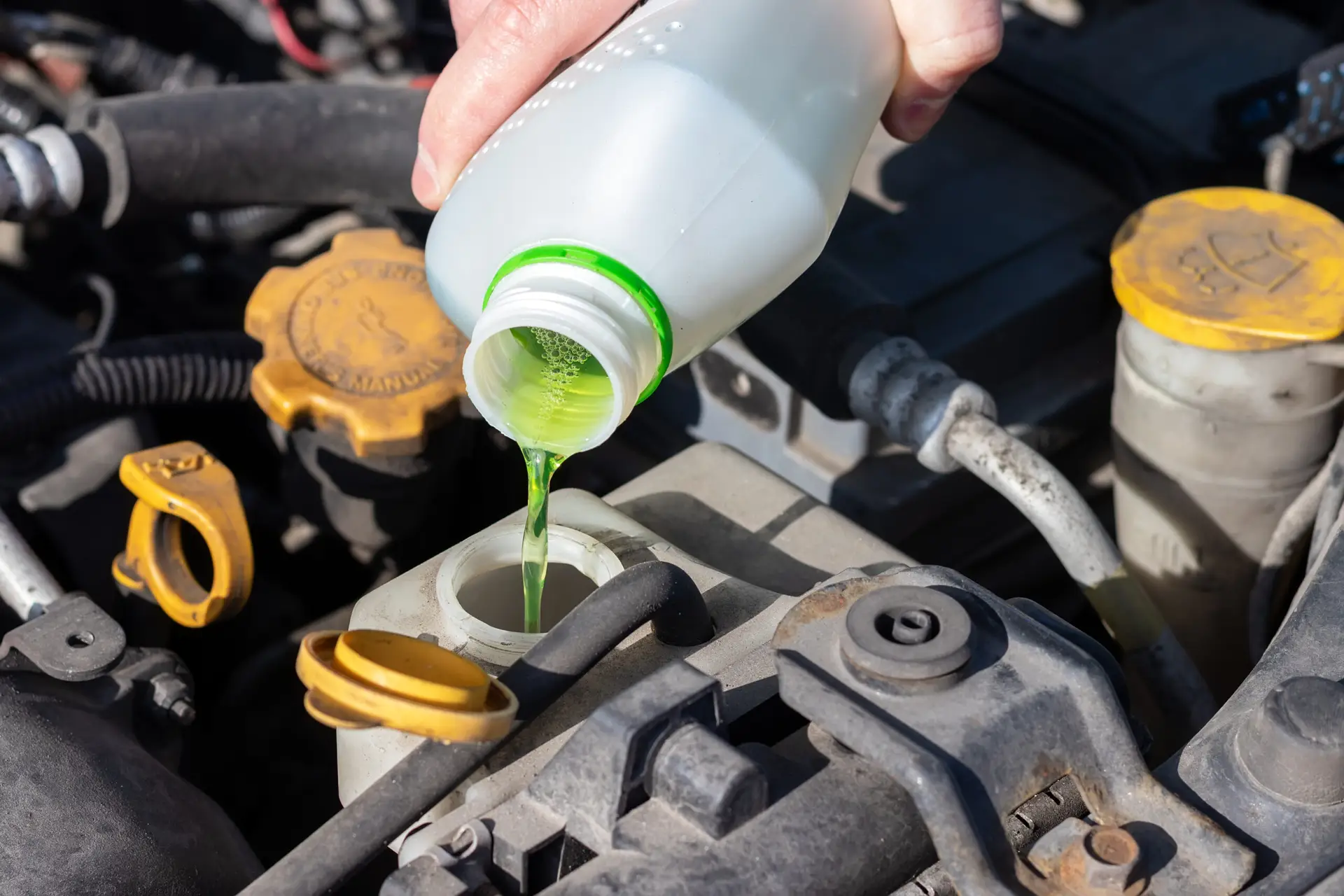 Hand with bottle pouring antifreeze coolant into the expansion tank. Dusty details of a flat-four (boxer) car engine compartment under the open hood. Closeup view on a sunny day